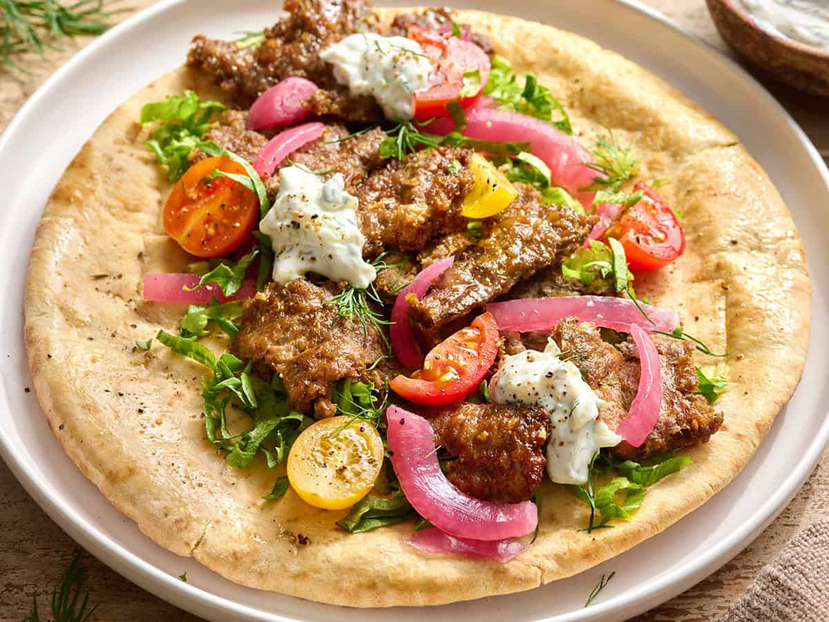 Overhead side view of a sheet pan doner kebab on a pita bead with salad and tzatziki sauce.