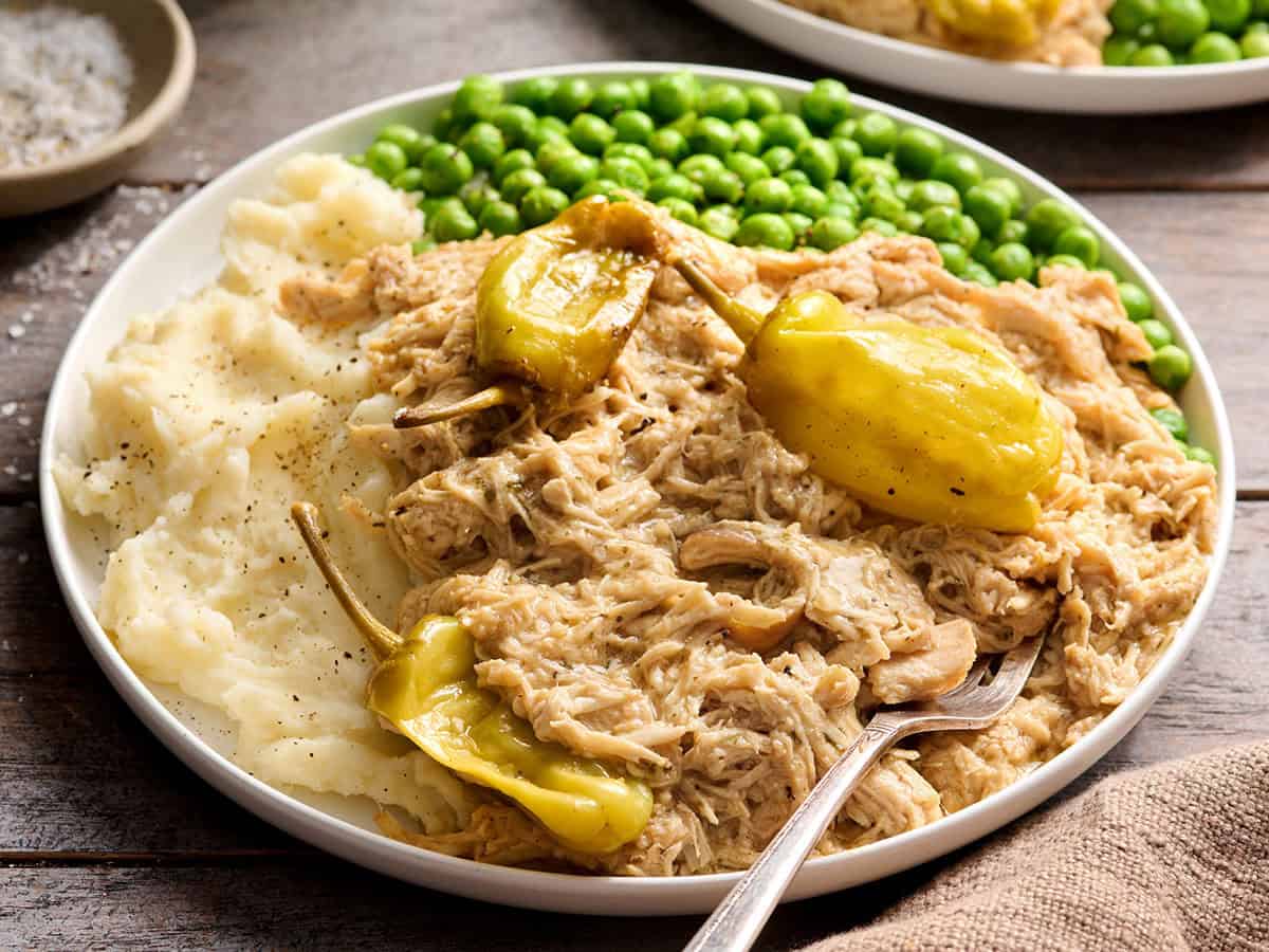 Mississippi chicken on a plate with mashed potatoes and green peas.