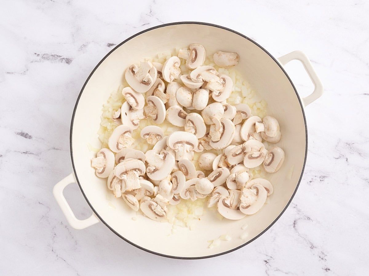 Mushrooms added to a skillet with sauteed onions.