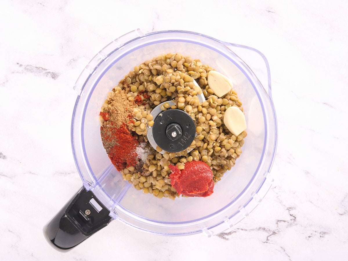 Cooked lentils, spices, tomato paste, and garlic in a food processor.