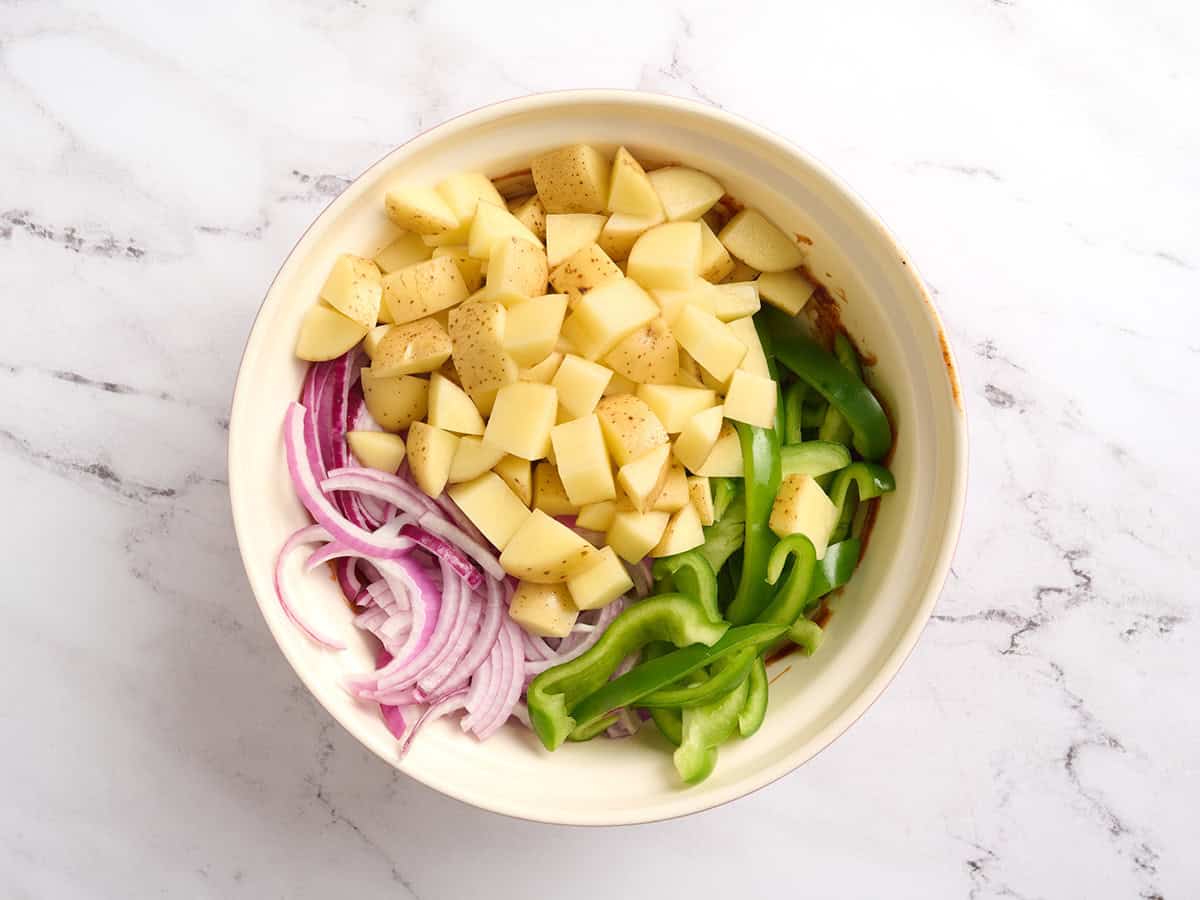 Sliced peppers, red onion, diced potatoes, and bbq sauce in a bowl.
