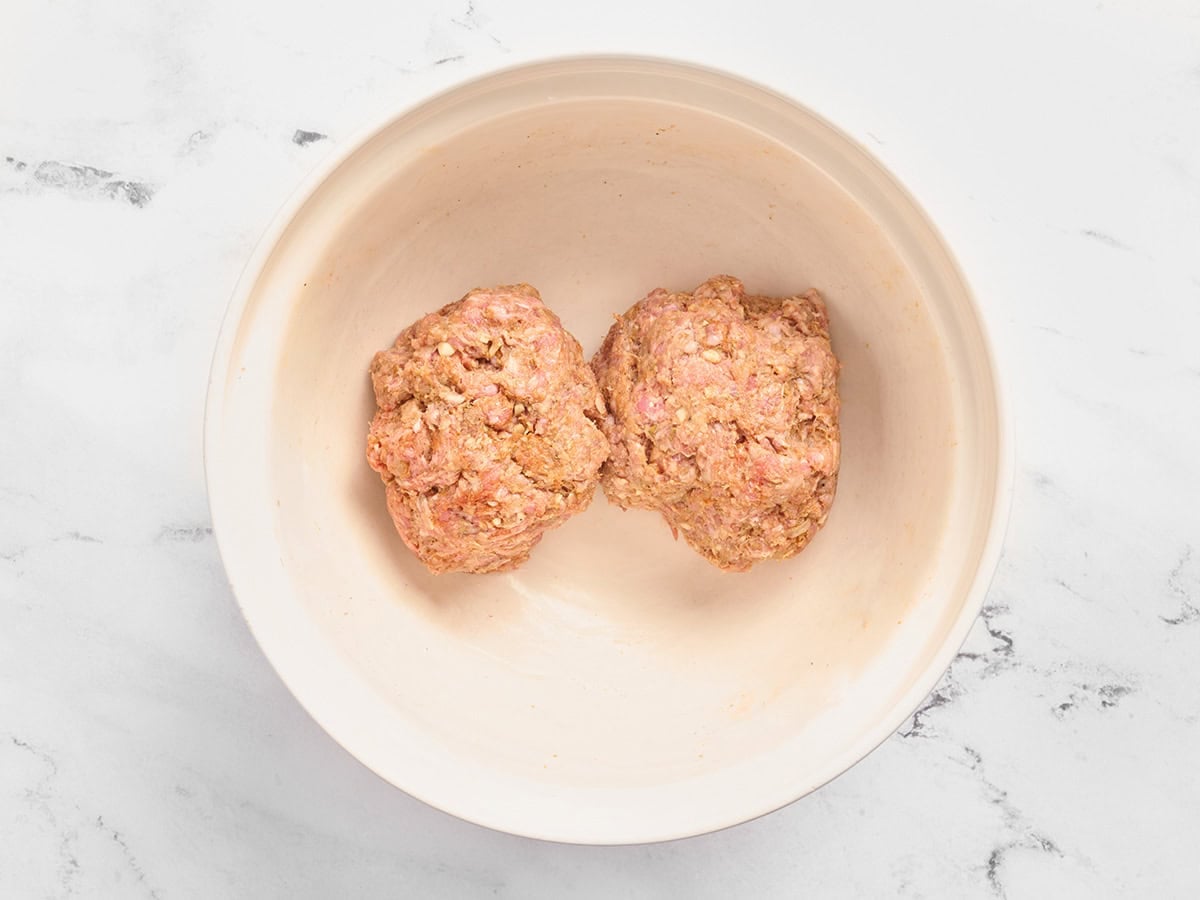 Two balls of seasoned ground beef in a bowl.