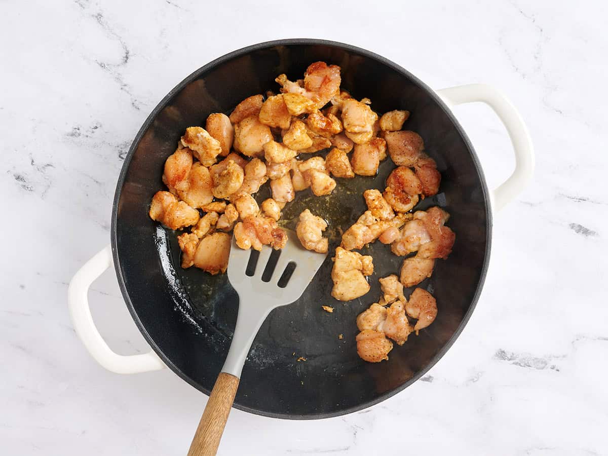 A spatula flipping chicken chunks in a skillet.