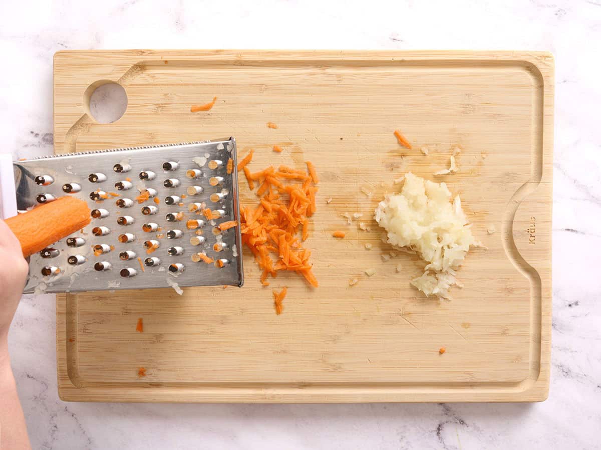 Grated carrot and onion on a wooden cutting board.