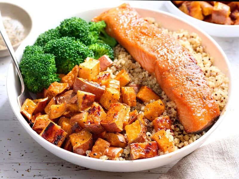 Front view of a bowl of quinoa with a salmon filet, roasted sweet potatoes, and broccoli.