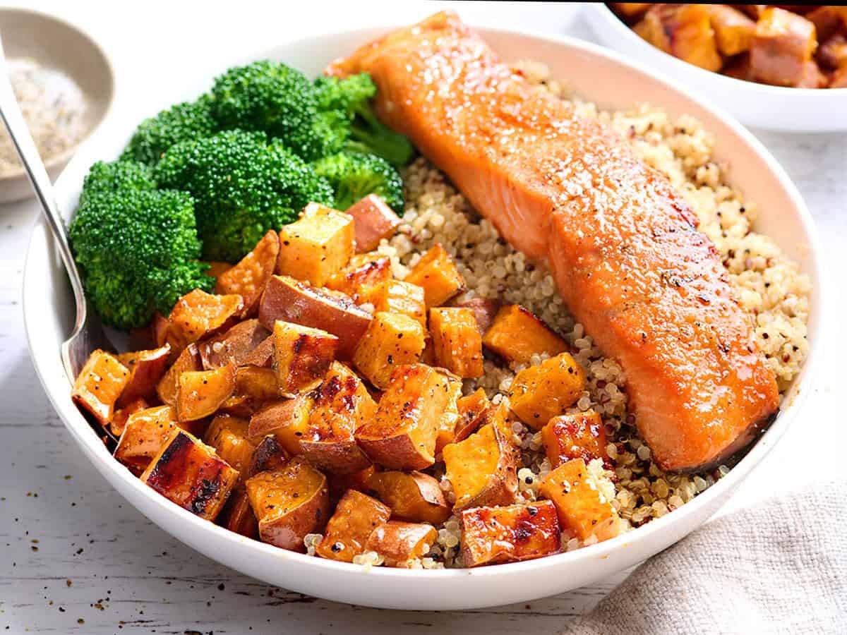 Front view of a bowl of quinoa with a salmon filet, roasted sweet potatoes, and broccoli.