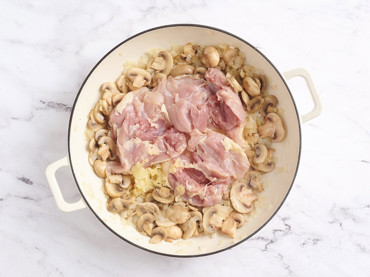 Chicken thighs added to a skillet with sauteed onions and mushrooms.