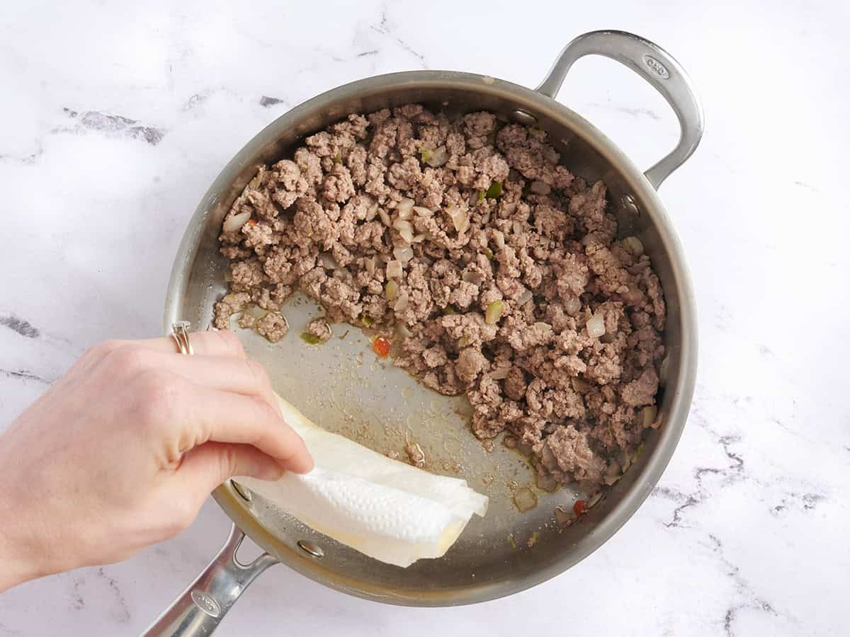 A hand using a paper towel to soak up grease from a skillet.