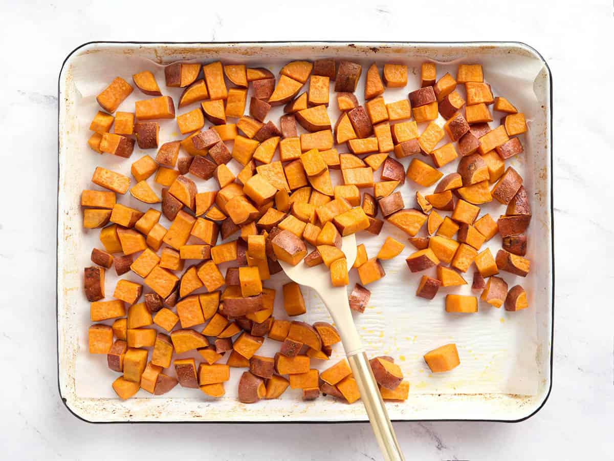 Sweet potato cubes on a baking sheet being tossed with a spatula.