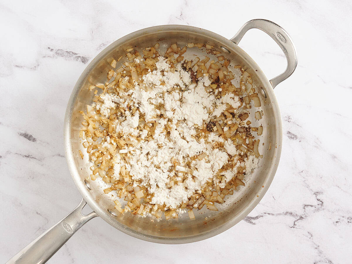 Flour added to a skillet of sauteed onions.