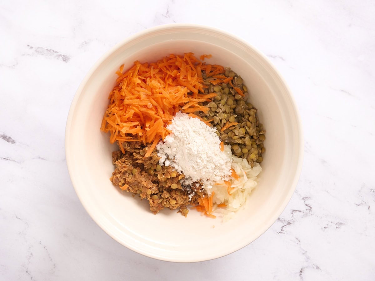 Grated carrots, lentils, blended lentil mix, flour and grated onion in a mixing bowl.