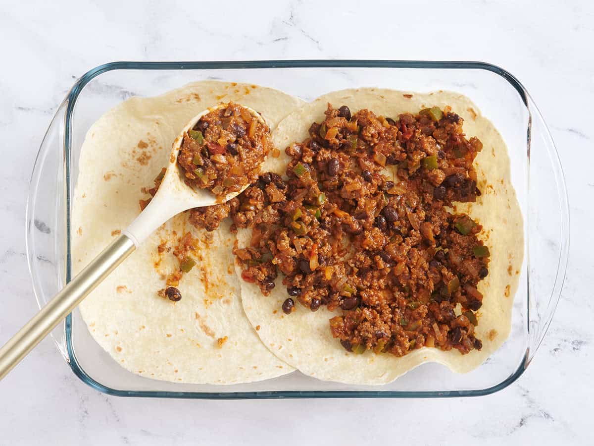 Tortillas layered in a baking dish with taco meat being layered over top.