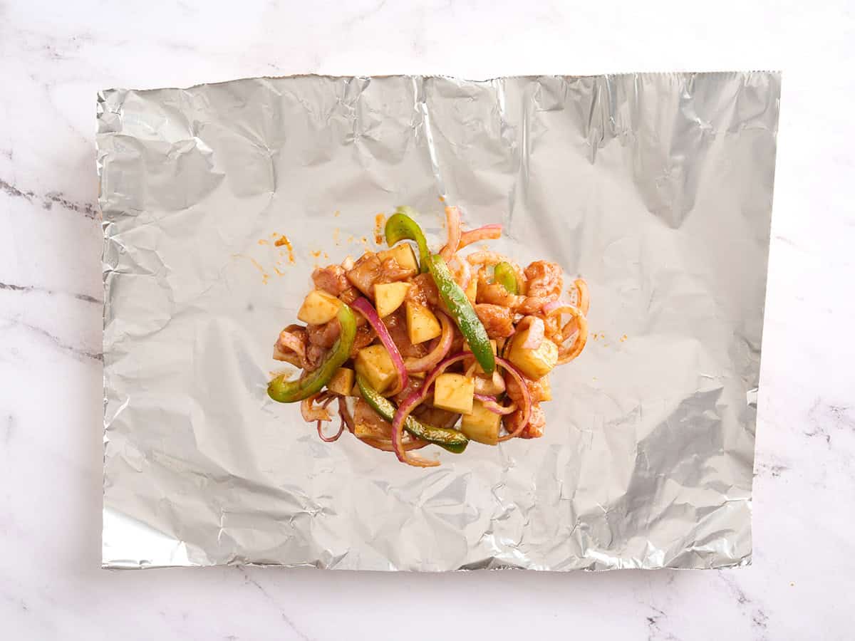 BBQ chicken, potatoes, peppers and onions on a sheet of foil.