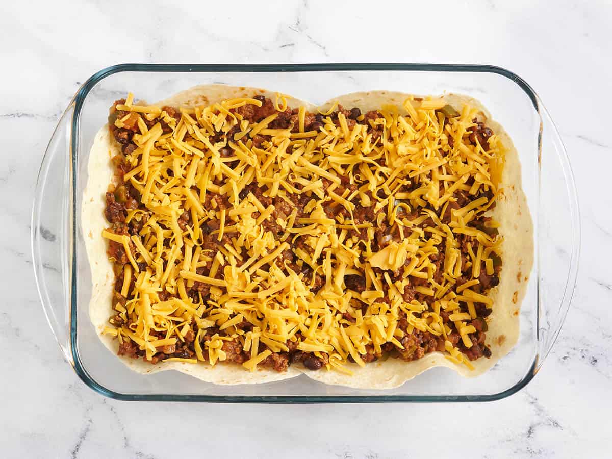 Cheese added to a casserole dish with taco meat and tortillas.