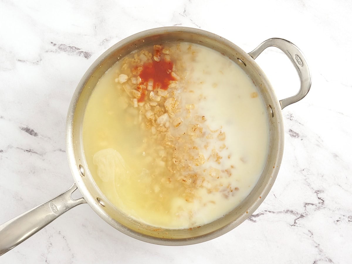 Chicken broth, milk, and hot sauce added to a skillet with onions.
