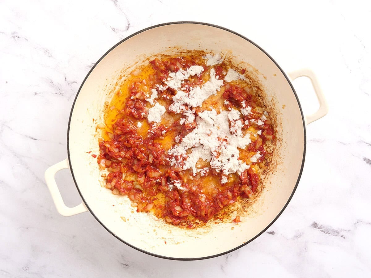 Flour added to a skillet with tomatoey onions to make a roux.