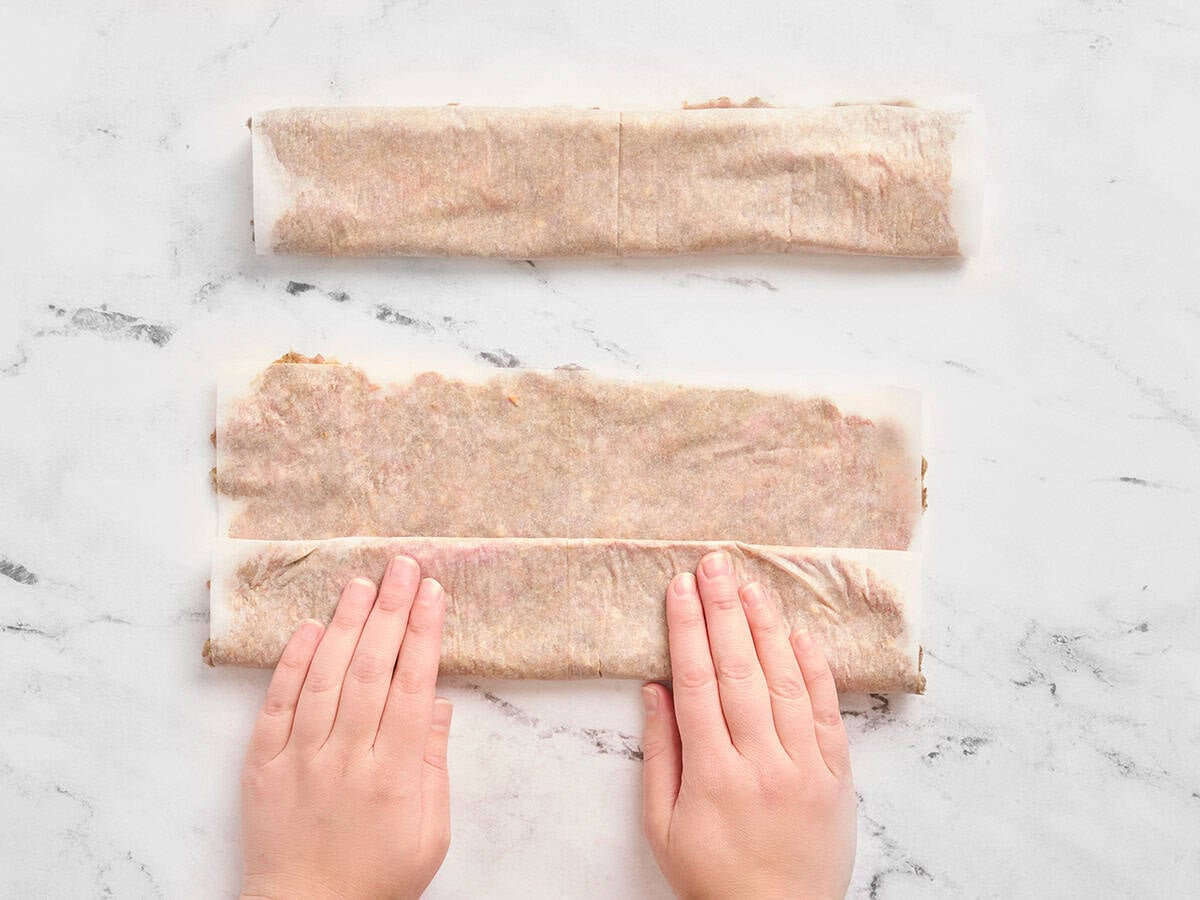 Hands rolling ground beef in parchment paper.