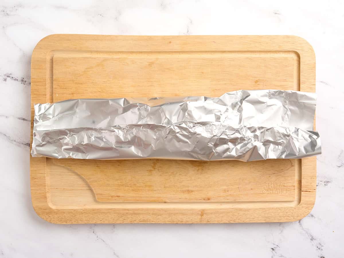 A foil packet folded in half on a wooden cutting board.
