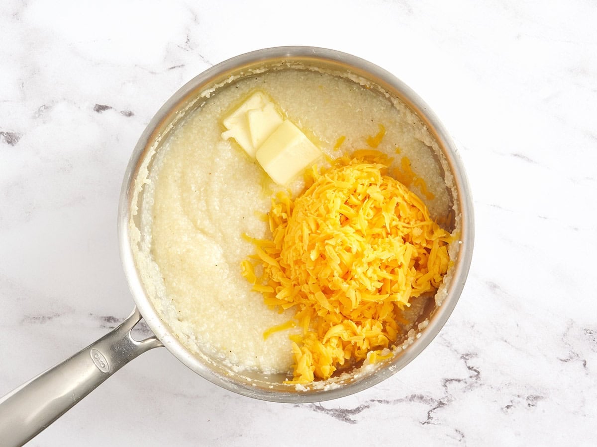 Shredded cheese and butter added to a pan of grits.
