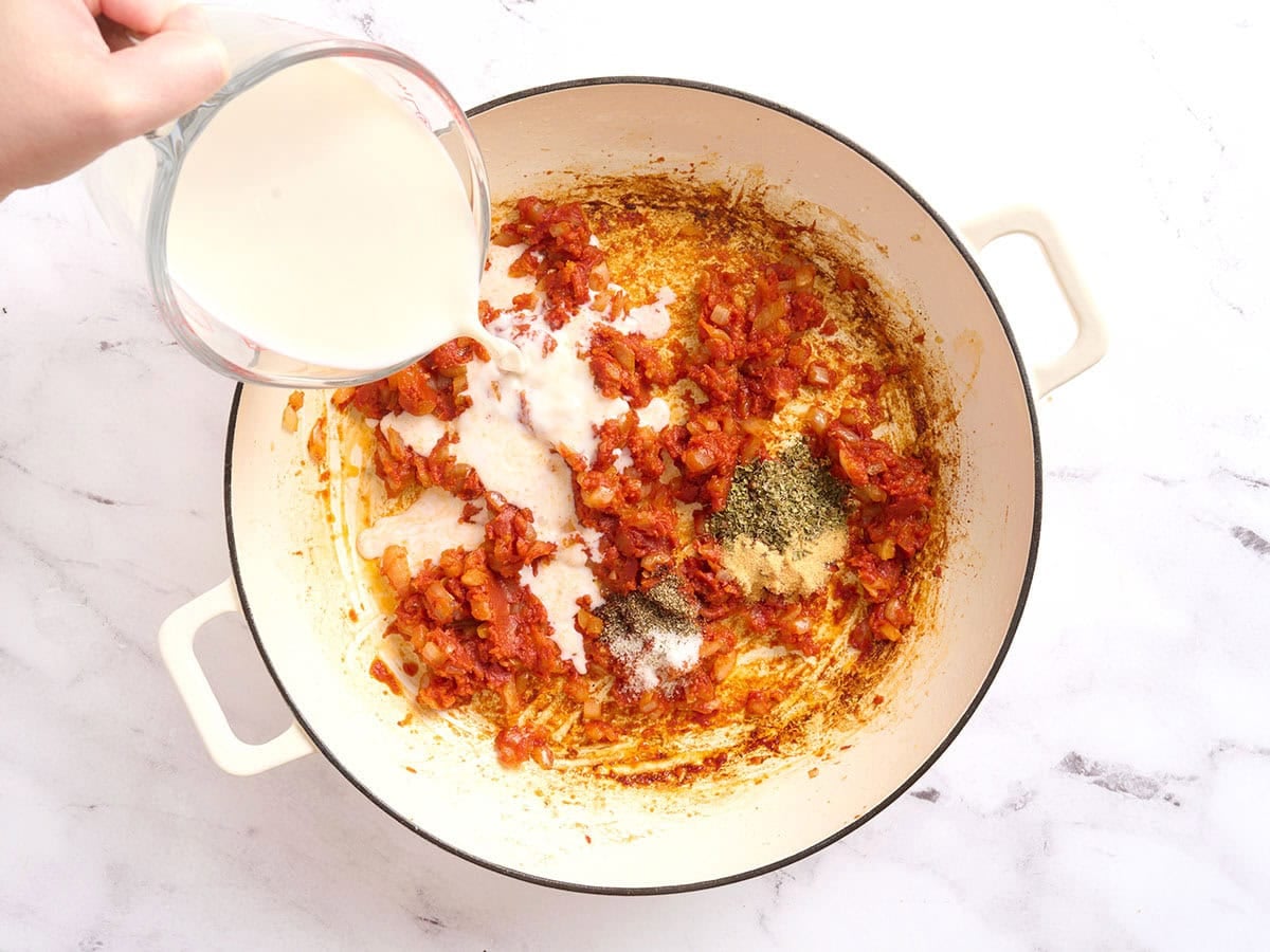 Milk being poured into a skillet to make a creamy tomato sauce.
