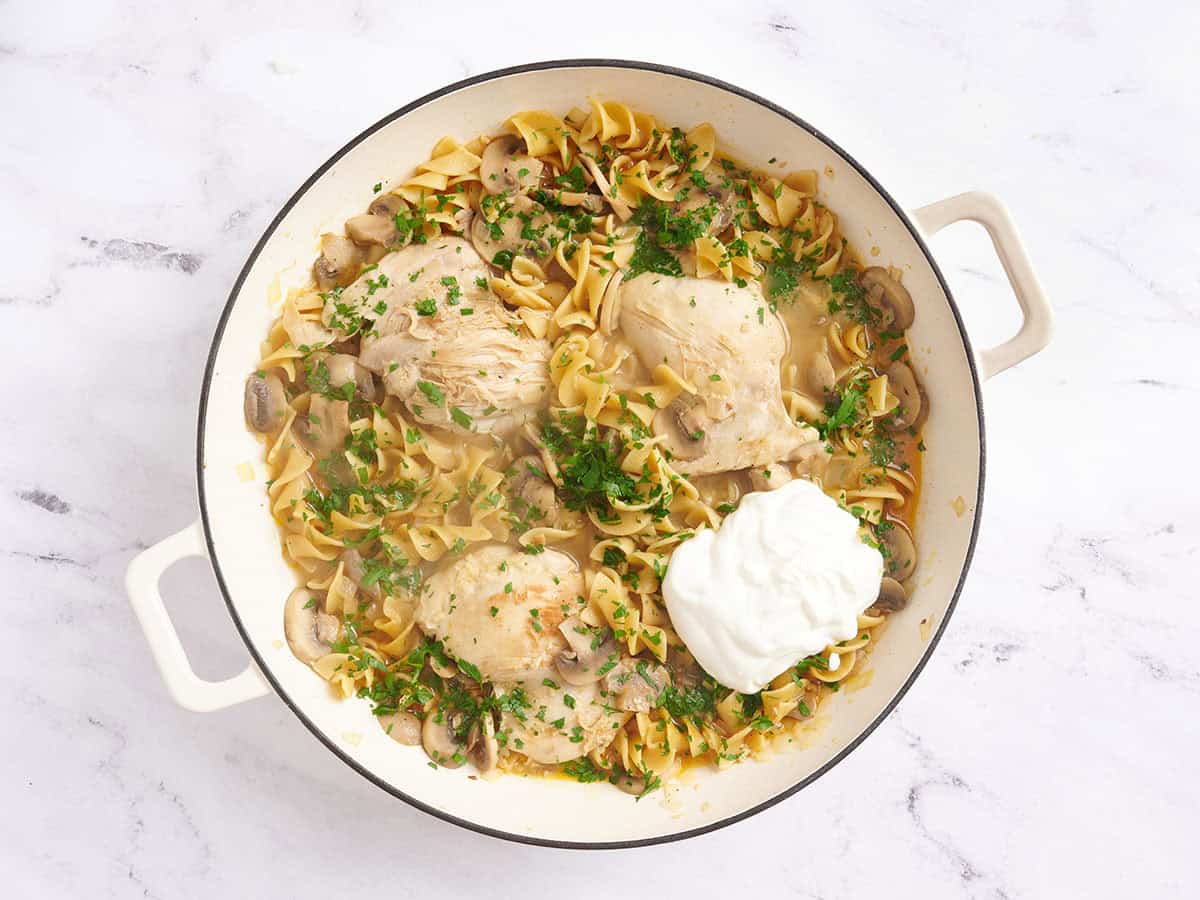 Sour cream and fresh parsley added to a skillet with chicken stroganoff.