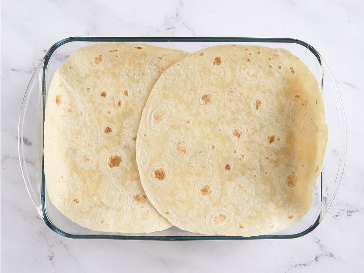Two large tortillas added to a baking dish.