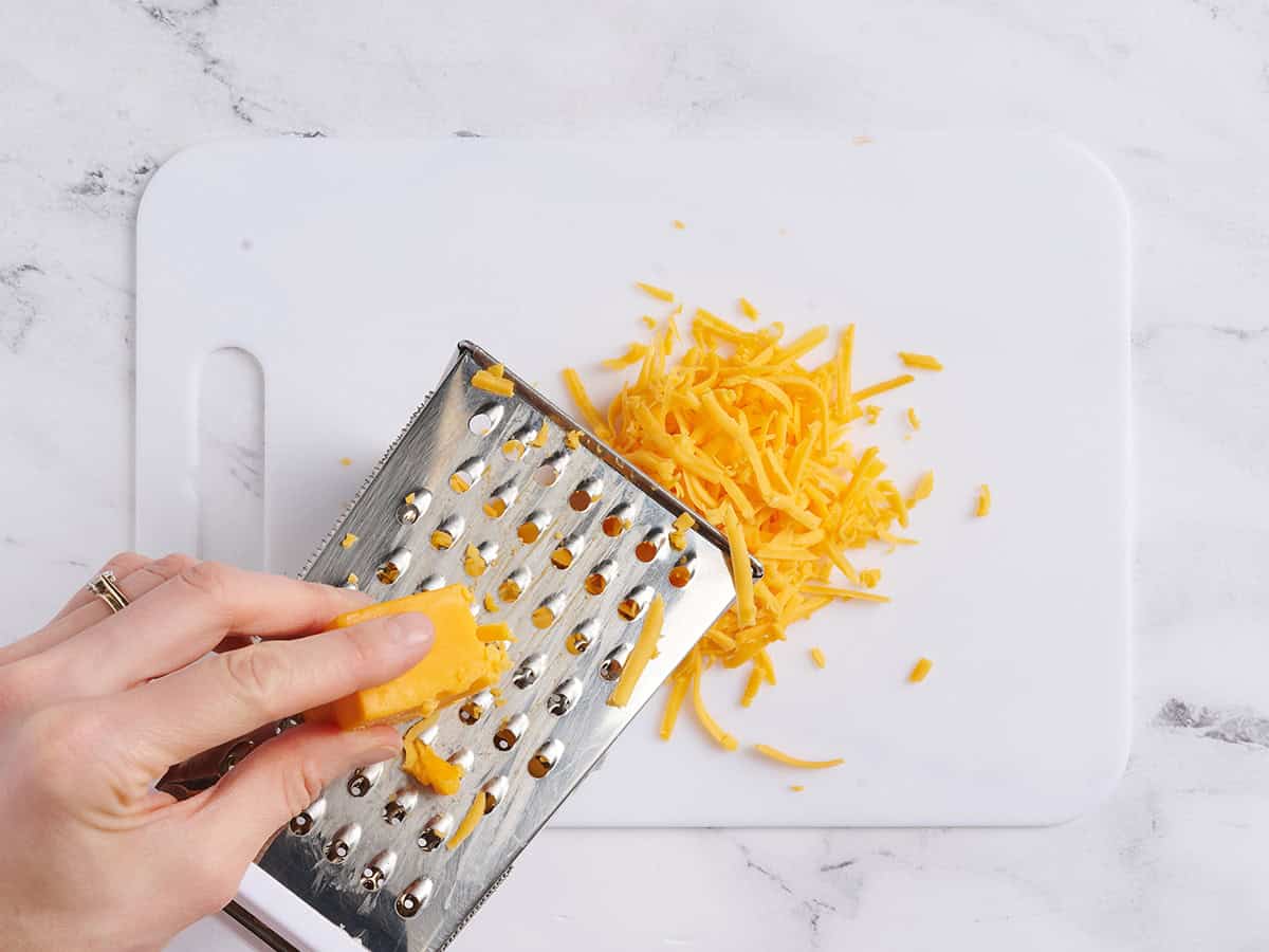 A hand using a box grater to shred cheese.