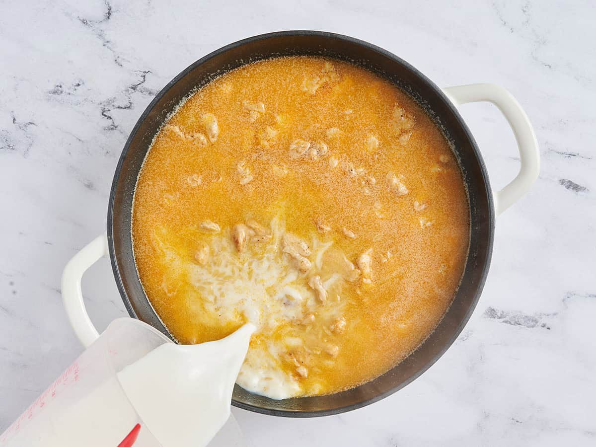 Milk being poured into a skillet with orzo, chicken and broth.