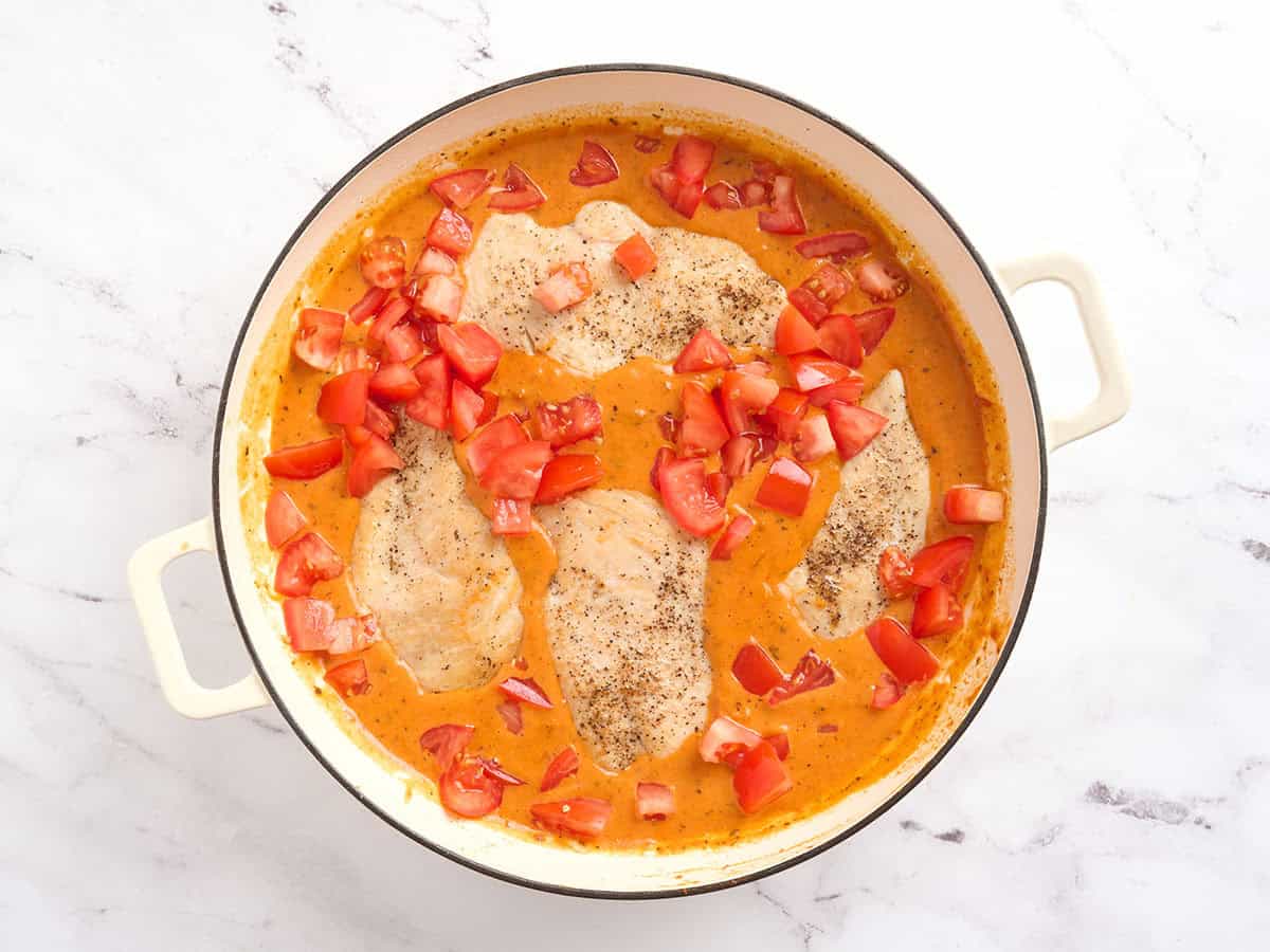 Diced tomatoes added to a skillet of creamy tomato chicken.