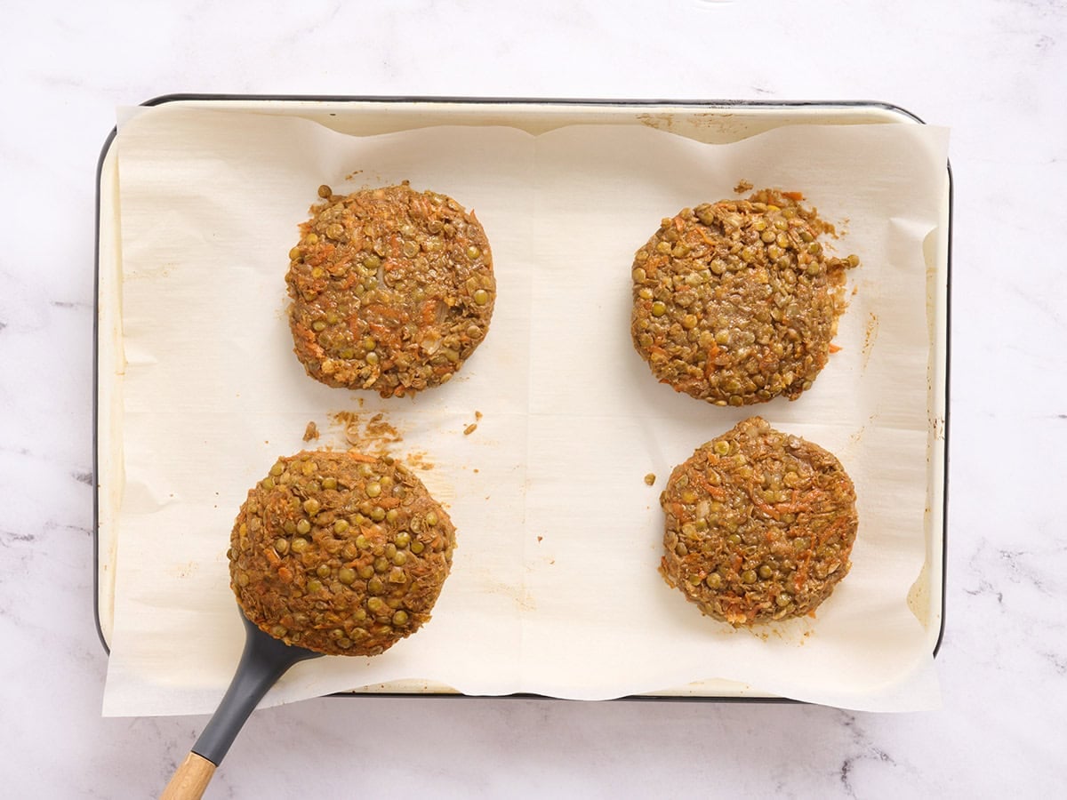 Lentil burgers on a sheet pan being flipped over halfway through cooking with a spatula.