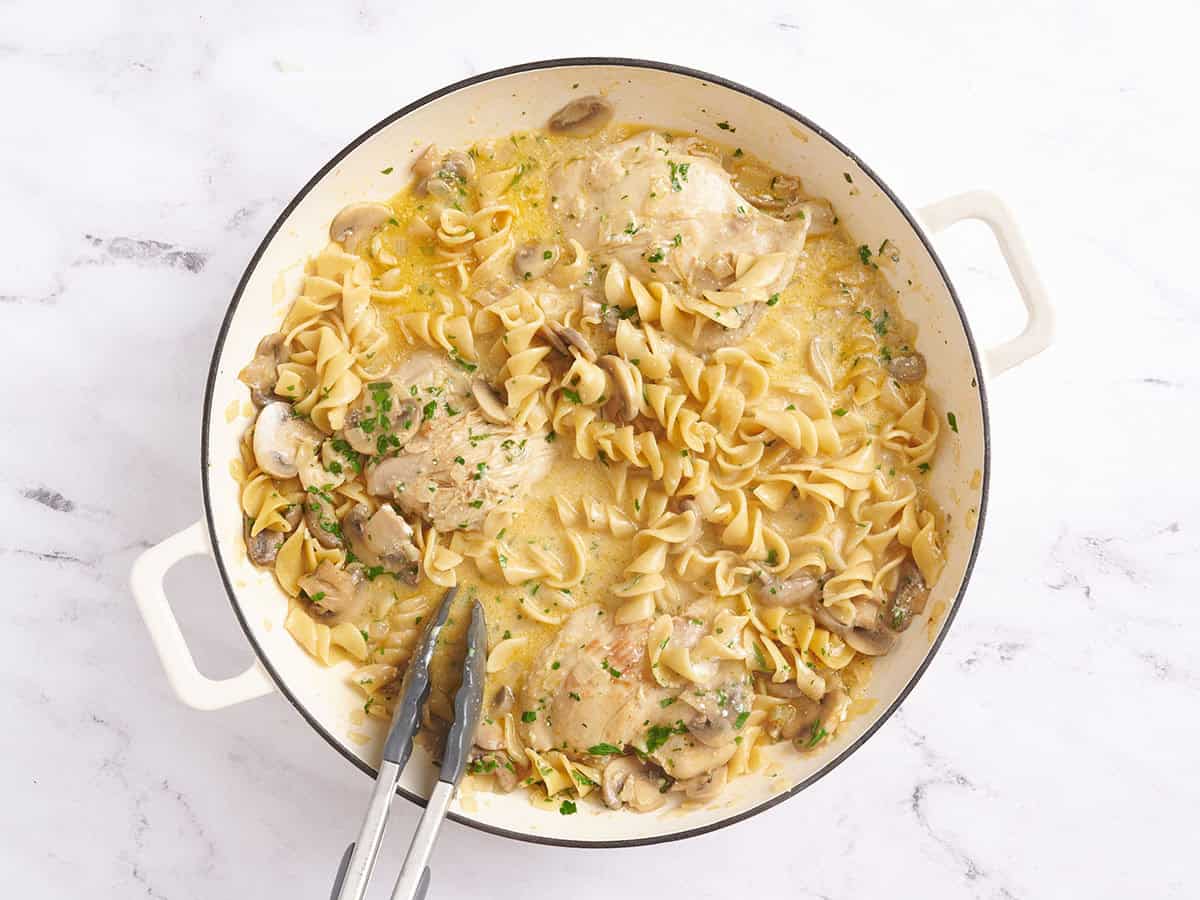 Chicken stroganoff in a skillet with kitchen tongs.