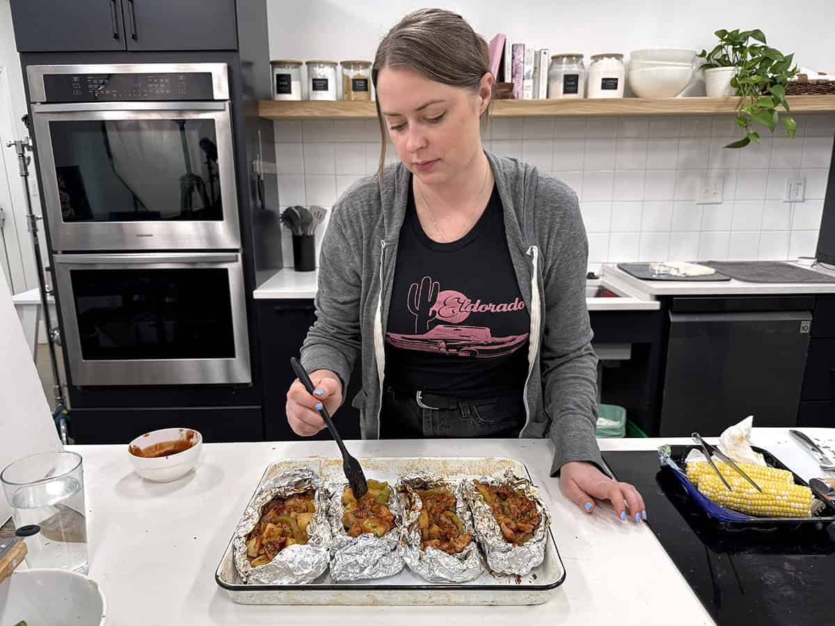 A women filling BBQ chicken foil packets in a kitchen.