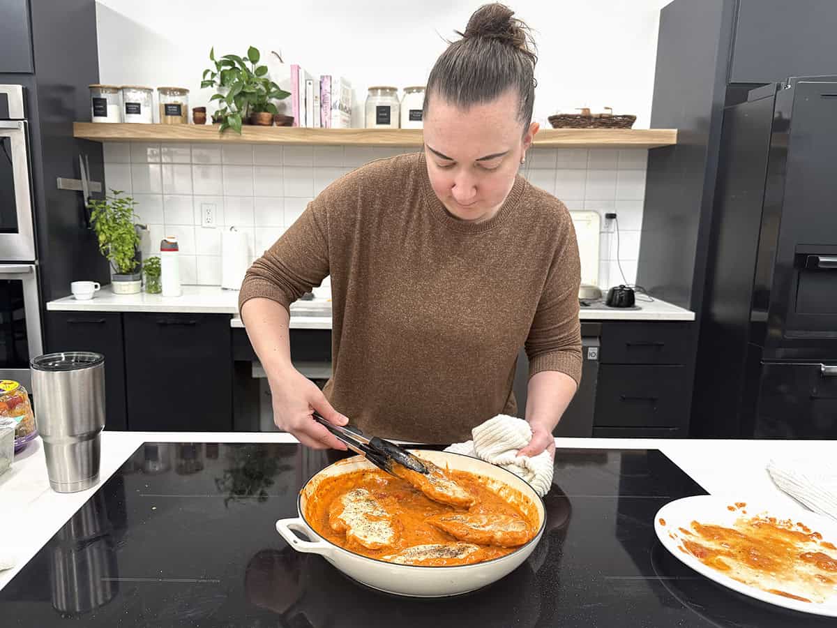 A women cooking creamy tomato chicken in a skillet.