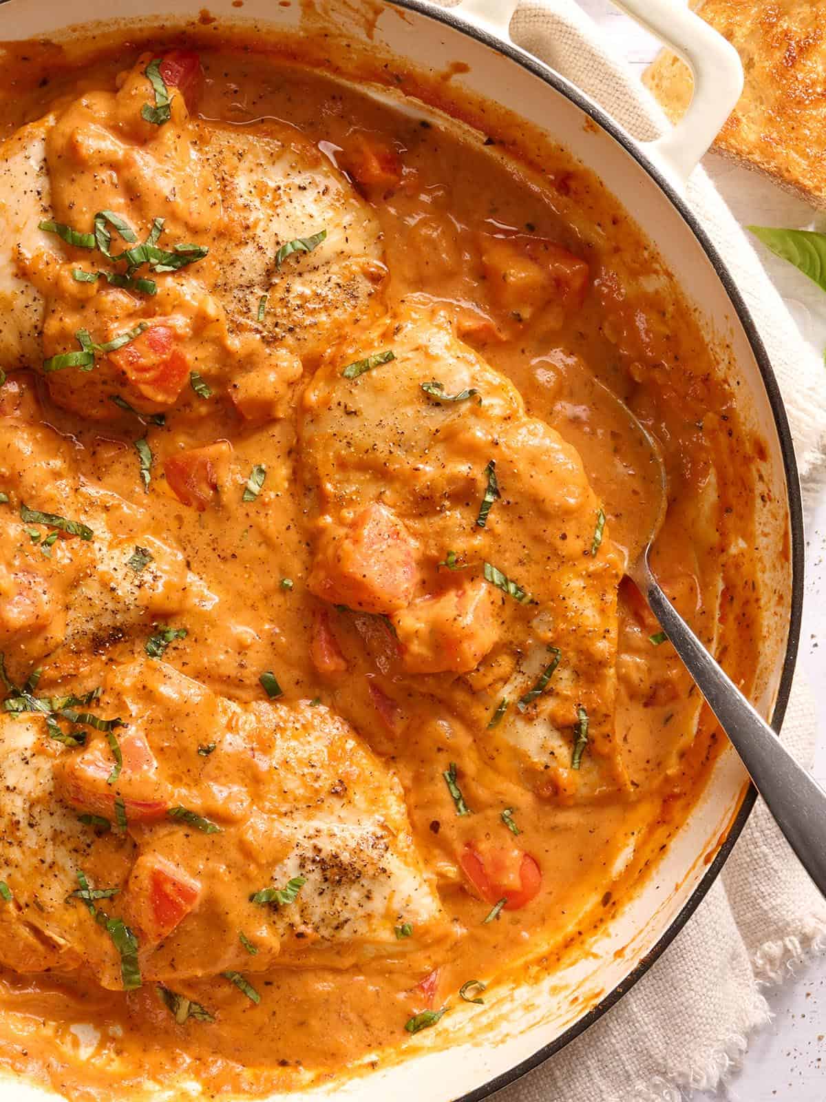 Overhead view of a skillet of creamy tomato chicken with a spoon.