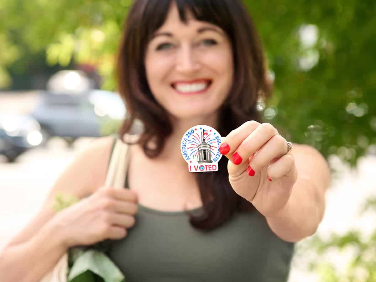 woman holding I voted sticker out smiling