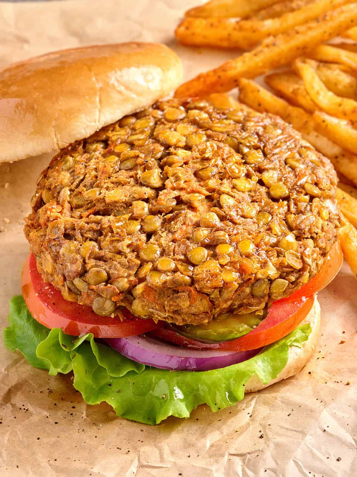 Overhead side view of a lentil burger in a hamburger bun, with salad and the top bun removed.