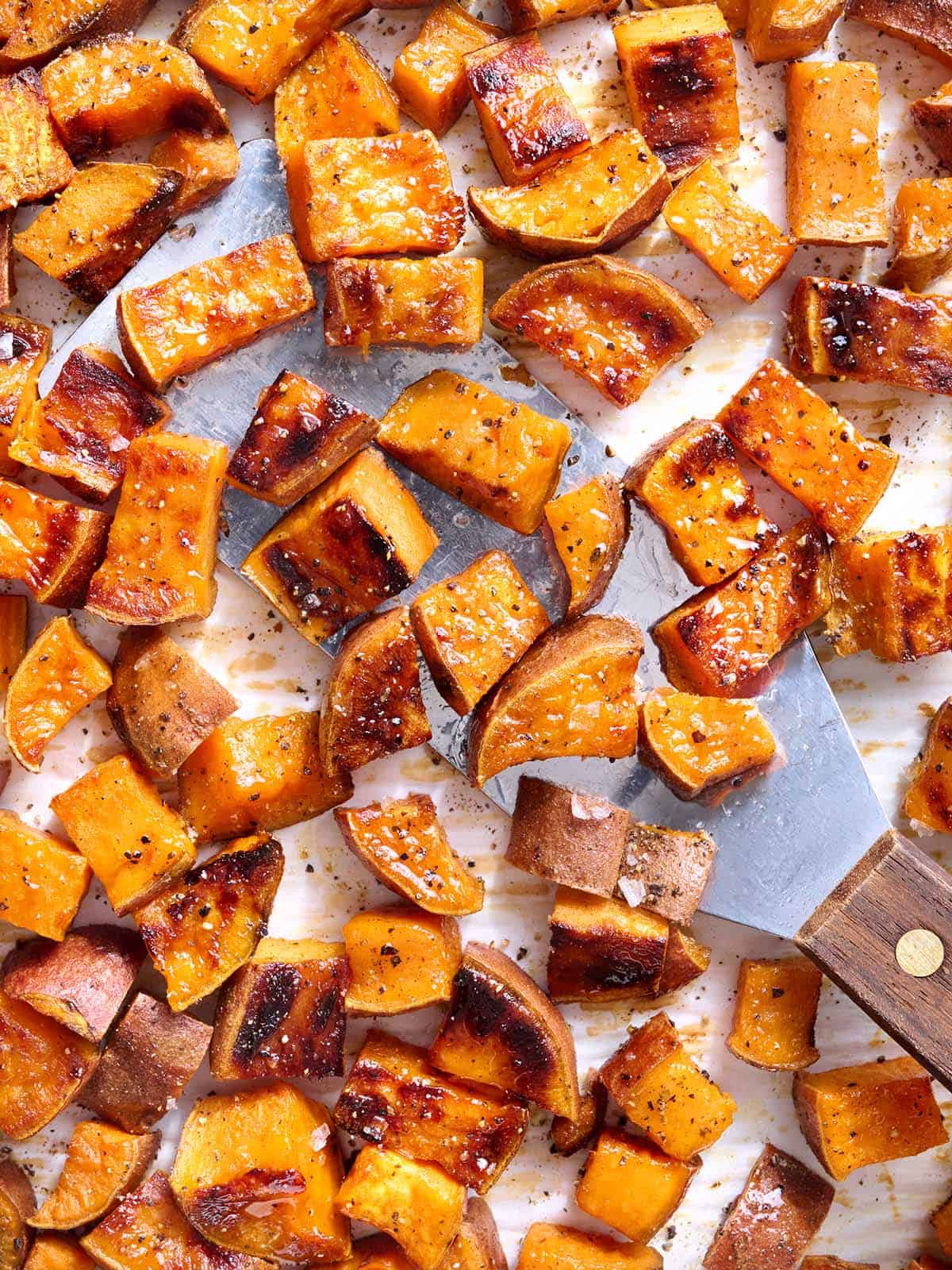 Overhead close up view roasted sweet potatoes with a metal spatula scooping some up.