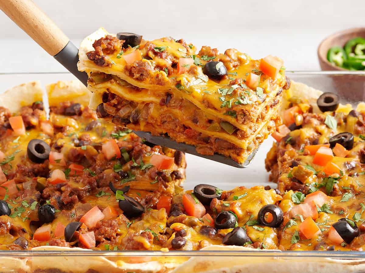 Side view of a slice of taco casserole being lifted from the baking dish.