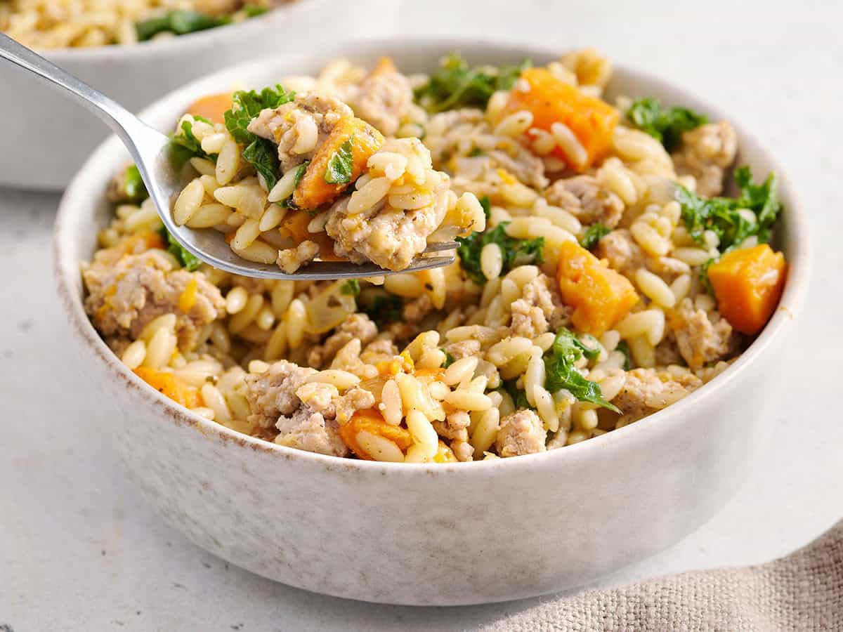 Side view of sweet potato and ground turkey orzo in a bowl with a knife taking some.