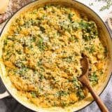 Overhead view of a skillet of creamy butternut squash orzo with a wooden spoon.
