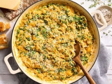 Overhead view of a skillet of creamy butternut squash orzo with a wooden spoon.