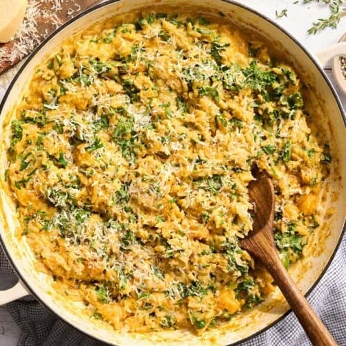 Overhead view of a skillet of creamy butternut squash orzo with a wooden spoon.