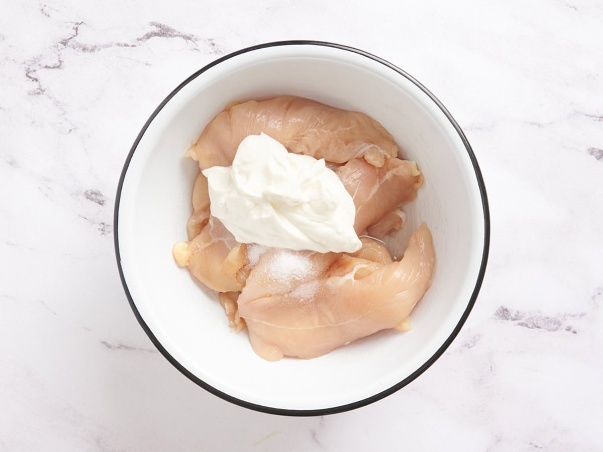 Chicken tenders, yogurt, water and salt in a mixing bowl.