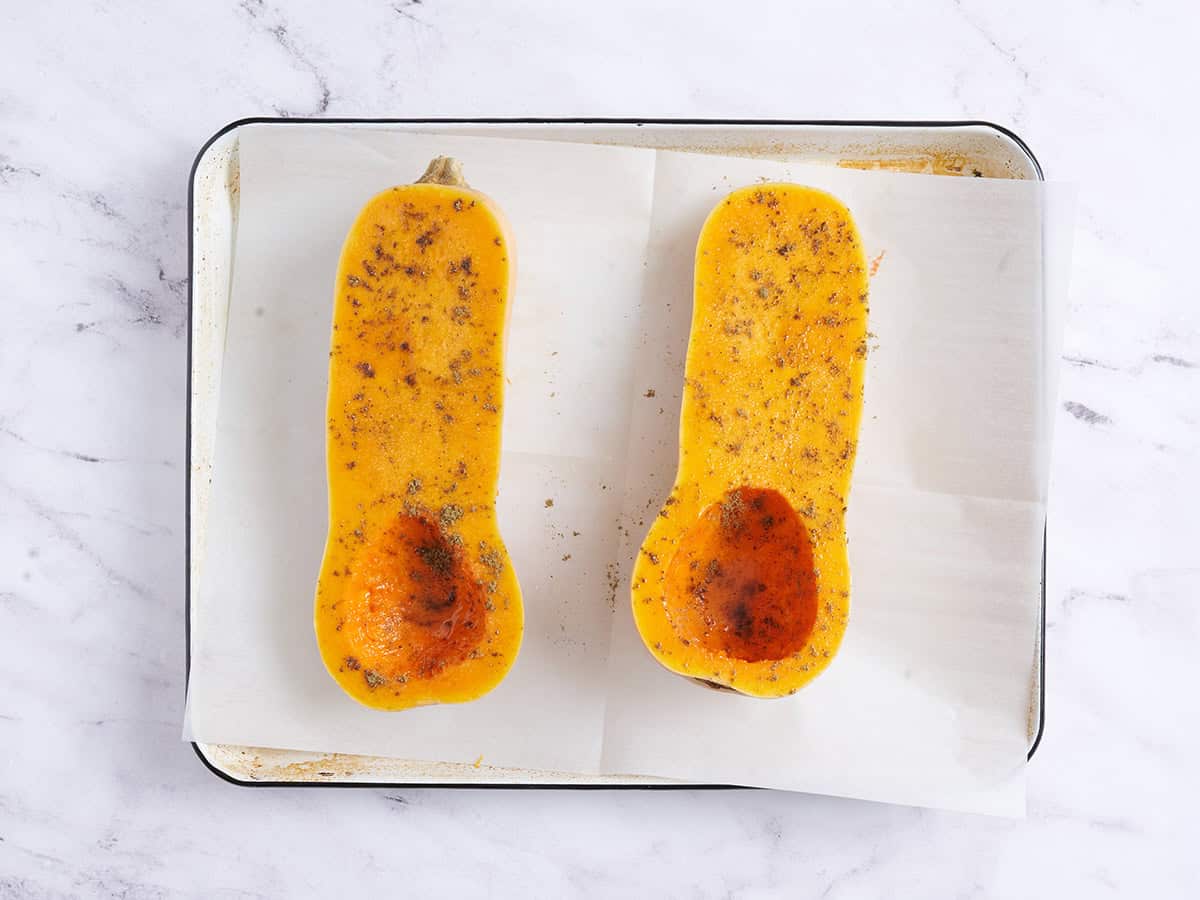 Seasoned butternut squash halves on a baking sheet before roasting.