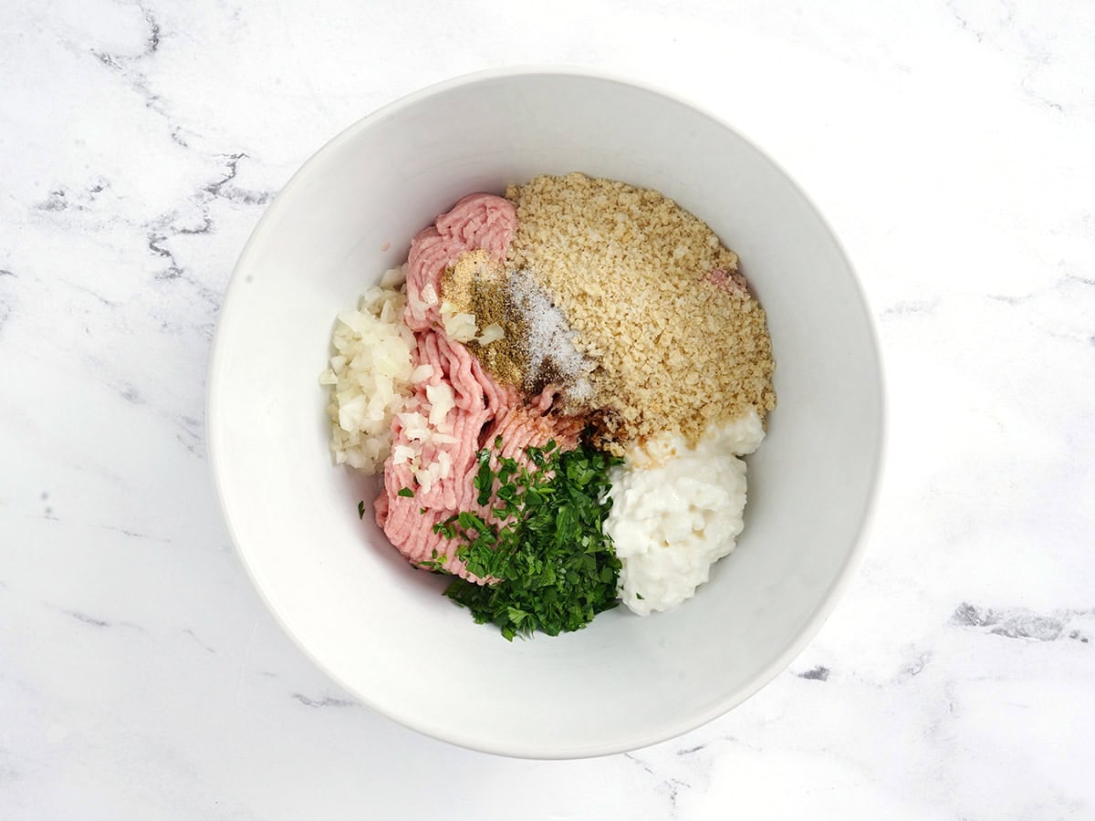 Ground turkey, panko breadcrumbs, cottage cheese, fresh parsley, and diced onion in a bowl.