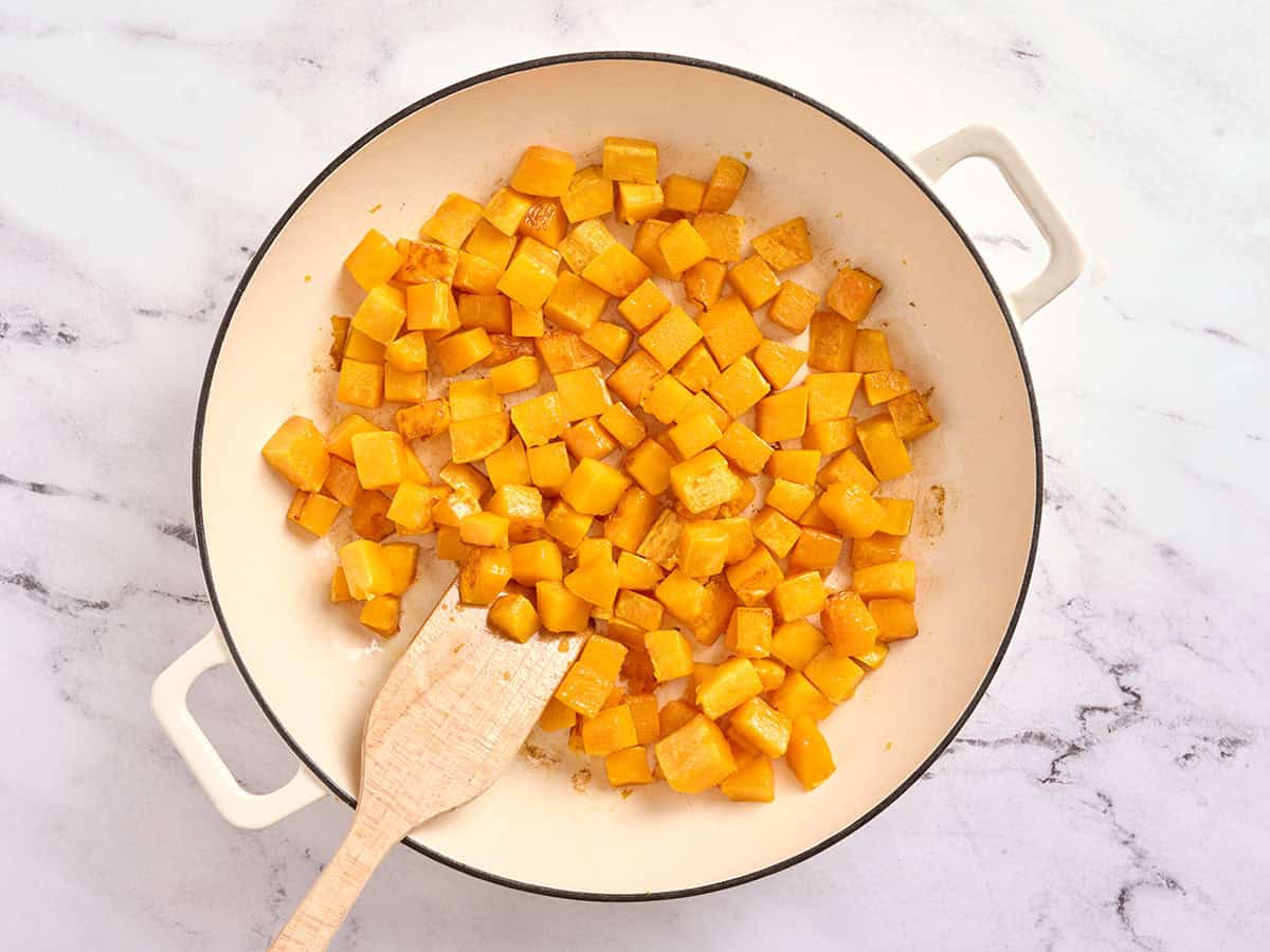 Dice butternut squash in a skillet with a wooden spatula.