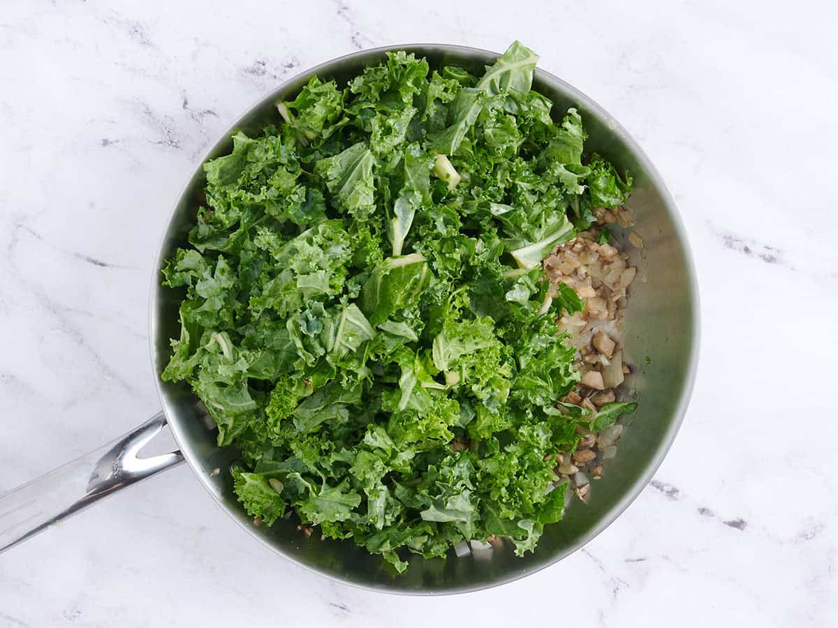Fresh kale added to a skillet with sauteed mushrooms and onions.