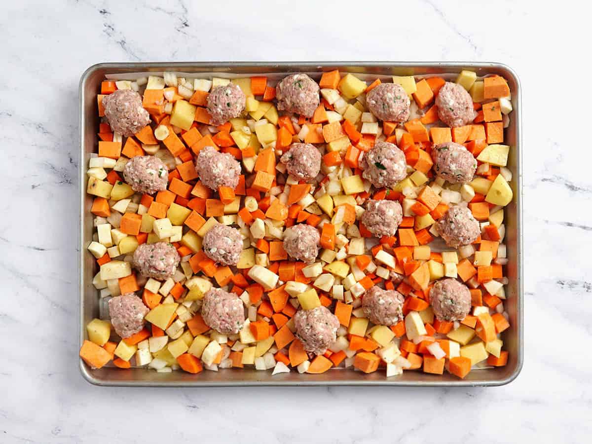 Shaped turkey meatballs added to a sheet pan with diced root vegetables.