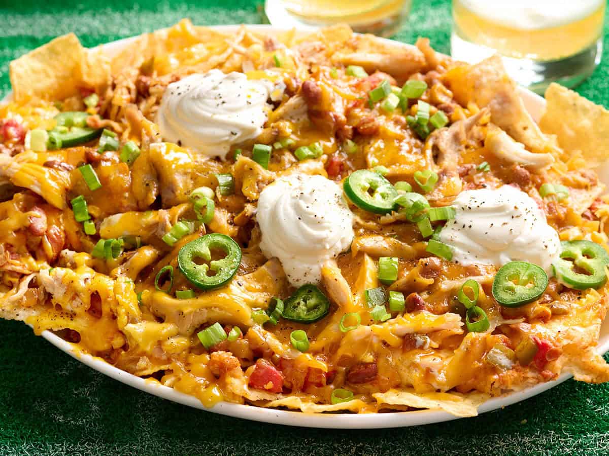 Side view of a platter of nachos topped with veggie chili, sour cream and jalapenos.