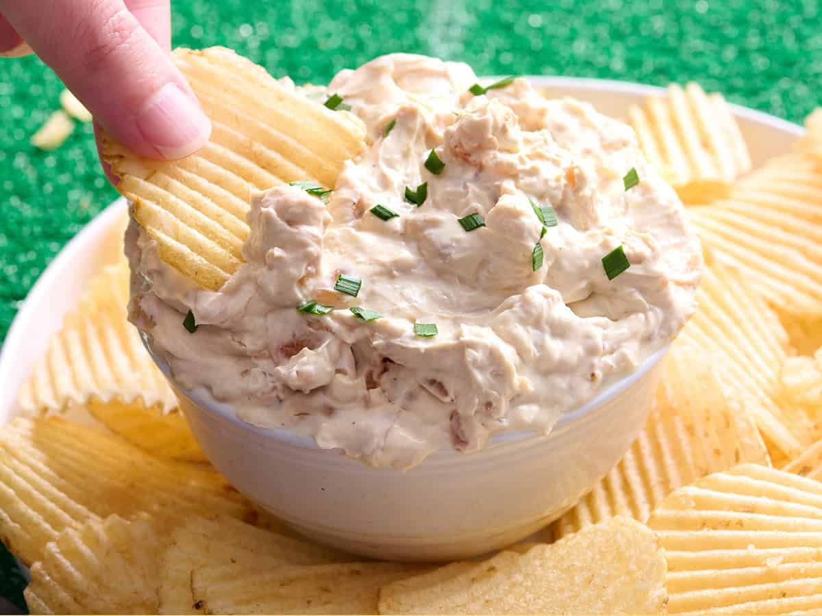 A hand dipping a chip into French onion dip.